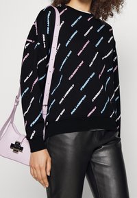 Felpa nera con motivo di testo colorato "KARL LAGERFELD". Presenta un collo rotondo e polsini a costine, abbinata a una borsa leggera di colore viola.