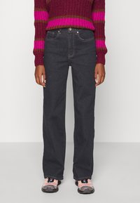 Mörka jeans med rak benmodell, utrustade med standardfickor och silverfärgad metalldetalj, kombinerade med en strukturerad tröja i magenta och brunt.