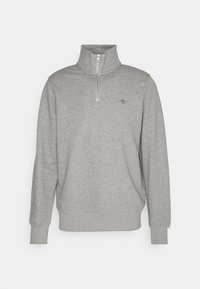 Pull gris clair à manches longues avec une fermeture éclair quart de zip et un col haut, avec un petit logo brodé sur la poitrine gauche.