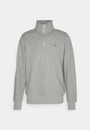 Sweatshirt gris en tissu doux, avec un col haut à demi zip, des manches longues et un petit logo brodé sur la poitrine.