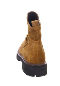 Botină din suede maron cu o talpă exterioară neagră robustă, cu un fermoar pe lateral și un logo pe toc. Textură netedă cu un finisaj mat.