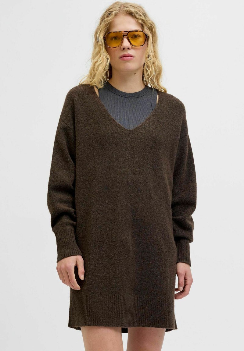 Vestido de punto tricotado en marrón oscuro con cuello en V, mangas largas, puños y dobladillo acanalados, con aberturas en los hombros. Textura suave.