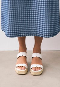 Witte espadrille-sandalen met een vierkante neus, een geweven jute zool en verstelbare enkelbandjes. Gdraag met een blauw-wit geruit rokje.