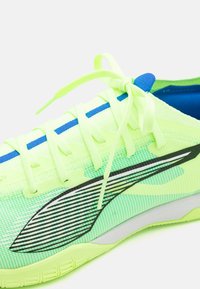 Scarpa da atletica verde neon con tomaia in rete, accenti blu, strisce nere e lacci piatti, dotata di suola testurizzata e colletto imbottito.