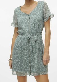 Grünes Polka-Dot-Kleid mit kurzen, flatternden Ärmeln, V-Ausschnitt, durchgehender Knopfleiste und einem Stoffgürtel. Leichtes, fließendes Material mit weicher Textur.