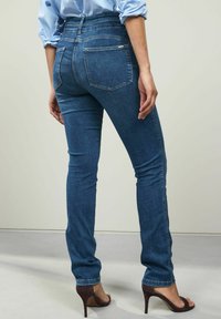 Vaqueros de denim de tiro alto y corte ajustado en azul oscuro con dos bolsillos traseros, costuras sutiles y una textura suave. Combinados con tacones altos.