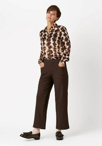 Printed, long-sleeve blouse in browns and creams; brown, wide-leg trousers; glossy, dark shoes; minimalistic design and structured fit.