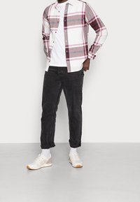 Camicia a quadri bianca, rosa e grigia; t-shirt bianca; pantaloni scuri; sneakers bianche con accenti chiari; indossato con calzini bianchi.