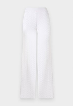 Weiße weite Hose mit dezentem Chevron-Strukturmuster und elastischem Bund vor einfarbigem Hintergrund.