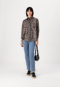 Leopard-print shirt made of fabric, featuring a collar and button closure, paired with light blue straight-leg jeans and black sneakers.