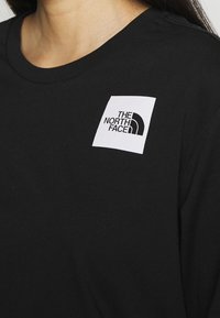 Primer plano de una persona que lleva una camiseta negra con un logo cuadrado blanco que presenta el texto "THE NORTH FACE" en el pecho.