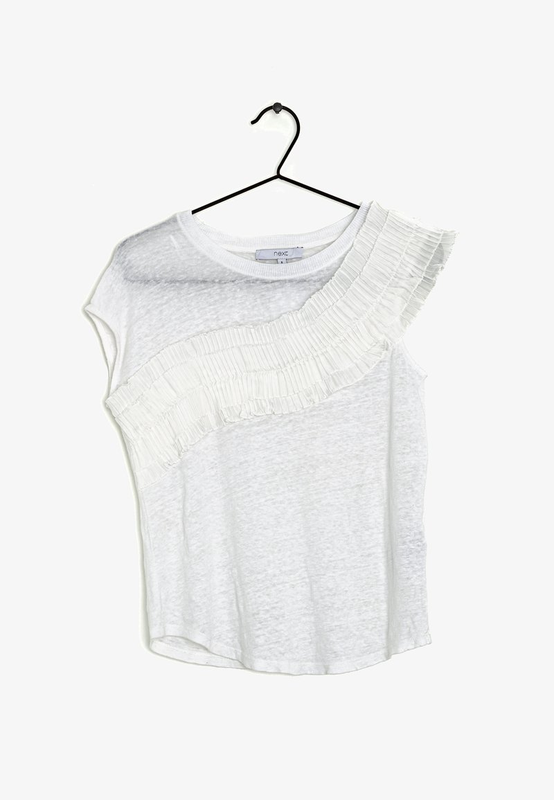 Haut à manches courtes blanc avec un détail froncé texturé et plissé le long d'une épaule. Fabriqué en tissu léger et légèrement transparent. Suspendu à un crochet noir.