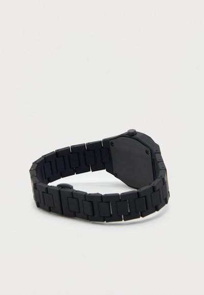 Μαύρο μεταλλικό ρολόι χειρός με συνδεδεμένο λουράκι, στρογγυλό κόρονα και πίσω μέρος θήκης σταθεροποιημένο με βίδες, εμφανιζόμενο από την εσωτερική πλευρά σε απλό φόντο.