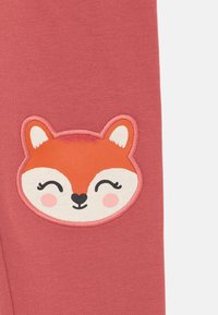 Rosa Baumwollleggings mit einer aufgenähten lächelnden Fuchs-Applikation und gestickten Details, einschließlich weißer und oranger Akzente im Gesicht.