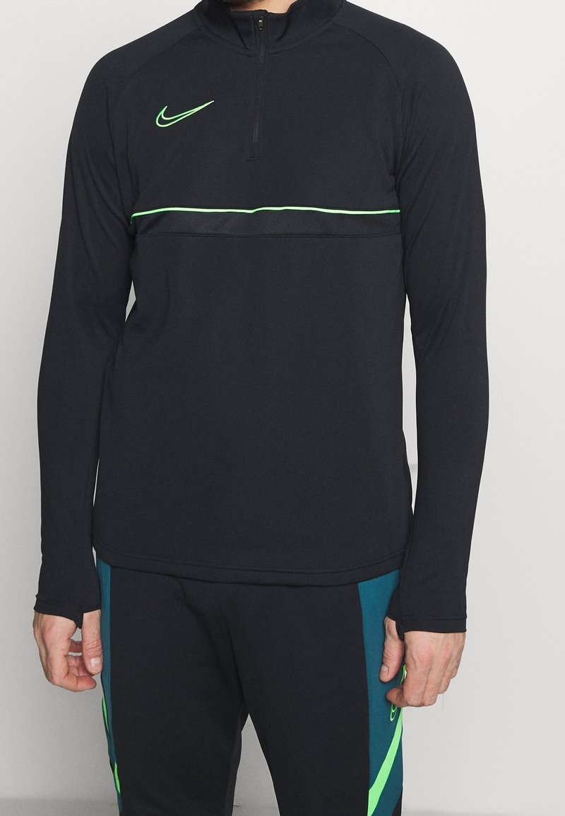 Černý atletický dlouhý rukáv s límcem na zip, zelenými akcenty a logem Nike na hrudi. Obsahuje horizontální zelený proužek.