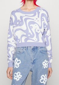 Lavender and white patterned sweater with a crew neck and ribbed hem, paired with light blue jeans featuring white floral designs.