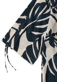 Détail de manche en tissu beige avec grand imprimé feuille tropicale bleu foncé et lien coulissant ajustable à l’ourlet.