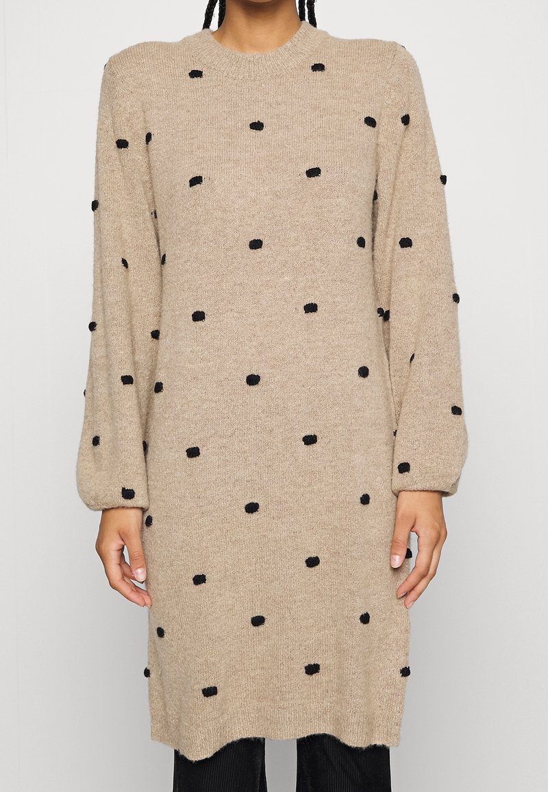 Robe pull beige en maille avec motifs à pois noirs, col rond, manches longues et poignets côtelés. Texture douce, coupe longueur genoux.