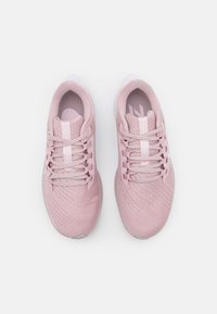 Zapatillas deportivas rosas con parte superior de malla texturizada, cordones planos y puntera reforzada. Detalles en blanco en la suela y en la marca, con una forma curveada.