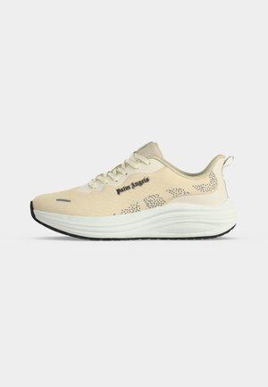 Beige Palm Angels-sneakers med hvid tyk sål, sorte mønstrede detaljer, snørebånd og trækstrop ved hælen på en ensfarvet baggrund.