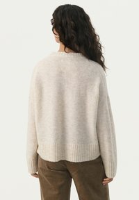 Pull oversized beige clair en tissu doux et texturé avec des poignets et un ourlet côtelés. Présente une coupe décontractée et un col rond.