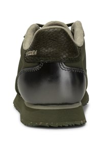 Zapatilla verde con un talón de malla negra texturizada, cuello gris suave y acentos de cuero negro brillante en la parte trasera. Suela de goma con textura antideslizante.
