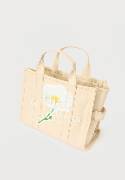 Béžová plátená taška s dvojitými vrchnými držadlami, s bielou grafikou gerbery a textom "THE TOTE BAG" vo vyvýšenej výšivke.