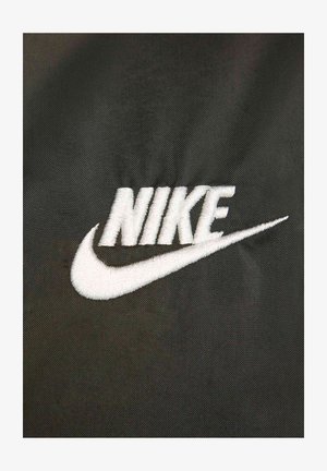 Biały haftowany logo "NIKE" na teksturowanym czarnym tle, z akcentem w postaci smugi wychodzącej z litery 'K'.