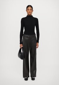 Svart turtleneck-genser, svarte skinnbukser med vide ben, og svarte sko; en svart håndveske holdes i venstre hånd. Enkelt design og glatt tekstur.