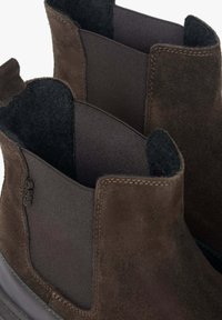 Brązowe zamszowe botki za kostkę z elastycznymi bocznymi panelami i miękką podszewką. Podeszwa jest czarna z fakturowanym gumowym wykończeniem.