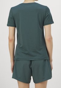 Tmavě zelené sportovní tričko s krátkým rukávem, hladkou texturou a kulatým výstřihem, v kombinaci s odpovídajícími kraťasy, které mají jednoduchý design.
