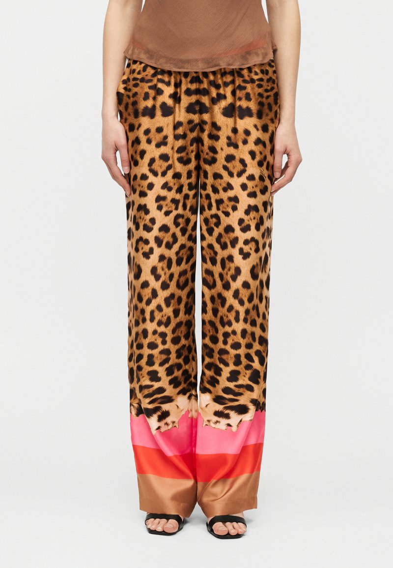 Παντελόνια με φαρδιά μπατζάκια με τύπωμα λεοπάρ στην κορυφή και μπλοκ χρωμάτων σε καφέ, κόκκινο και ροζ στο κάτω μέρος, φορεμένα με μαύρα σανδάλια με ανοιχτά δάχτυλα.