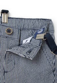 Marineblauwe en witte gestreepte tuinbroek met een metalen clip, knoopsluiting en een klein pocketdetail. De stof is textuur rijk en duurzaam.