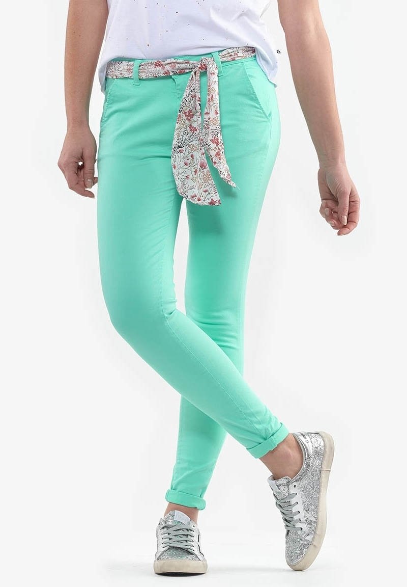 Mintgröna figursydda byxor med ett blommigt mönstrat knytbälte. Har en slät textur och uppvikt fåll. Matchas med sneakers i silverglitter.