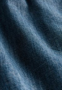 Nærbillede af denimstof, der har en rig blå farve med en struktureret overflade, som fremhæver fine vævemønstre og subtile variationer i nuancer.