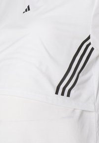 Hvit idrettsskjorte med svarte tre-stripes detaljer på ermene og et minimalistisk design. Myk, lett tekstur.