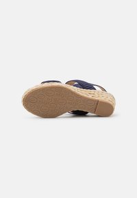 Marineblå espadrille-sandal med vevd tekstiloverdel og flettet jute-midtso. Gummiyttersålen har pregede sirkulære mønstre.