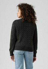Mörkgrå kabelstickad tröja med ribbad nederkant och muddar. Har ett strukturerat mönster, långa ärmar och en avslappnad passform.