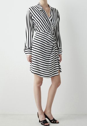 Woman wearing a black and white striped wrap dress with long sleeves and collar, paired with black open-toe heeled sandals.