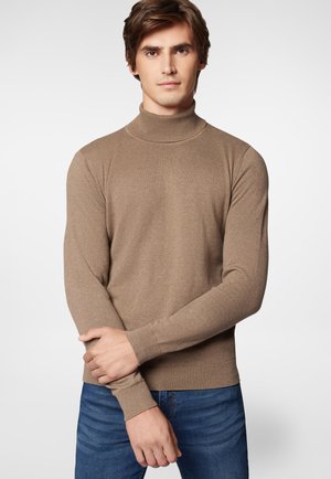 Brązowy sweter z golfem wykonany z miękkiej dzianiny, z długimi rękawami i ściągaczami. Noszony na niebieskie dżinsy.