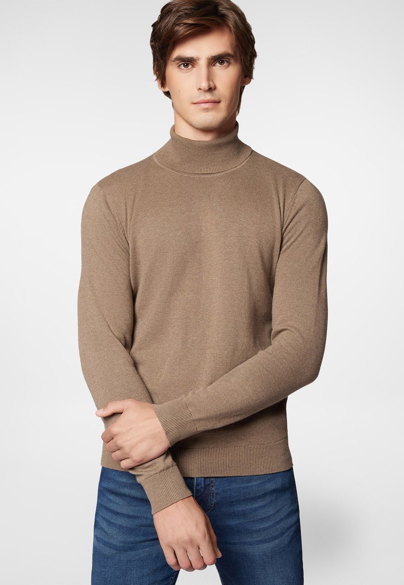 Brązowy sweter z golfem wykonany z miękkiej dzianiny, z długimi rękawami i ściągaczami. Noszony na niebieskie dżinsy.