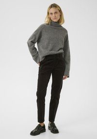 Harmaa neulottu korkeakauluksinen villapaita, rento malli, yhdistetty tummanruskeisiin corduroy-housuihin. Mustat kengät, joissa on tasapohja. Yksinkertainen, toimiva muotoilu.