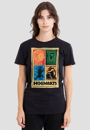 Young woman wearing a black Hogwarts t-shirt with colorful house animal symbols: lion, snake, eagle, and badger on a gray background.