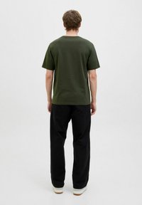 Mørkegrøn bomulds T-shirt med rund hals, korte ærmer og afslappet pasform, parret med løstsiddende sorte bukser og sko med hvid sål.