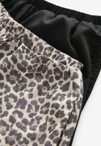 Zwei Shorts: eine aus schwarzem Stoff, die andere aus beigem Material mit einem grauen Leopardenmuster. Beide verfügen über einen elastischen Bund.