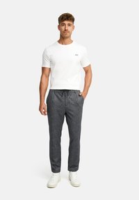 Hvit t-skjorte med rund hals og "JEFF" trykt i svart, sammen med mørkegrå innsnevrede bukser med snøring i livet og sidelommer.