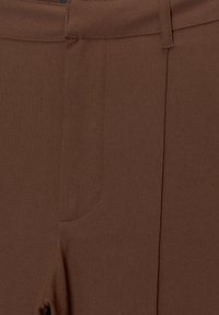 Pantalons en tissu texturé marron avec une taille lisse, comportant une poche unique et des détails de couture soignés.