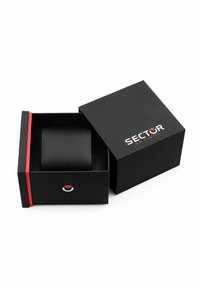 Scatola regalo nera con un design elegante, caratterizzata da una fascia accentuata rossa e un logo circolare sul fronte. Contiene un oggetto nero con una texture all'interno.