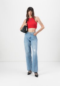 Top crop rouge, jeans taille haute bleu clair avec des déchirures, et chaussures à talons noires. Sac à main noir au design structuré.