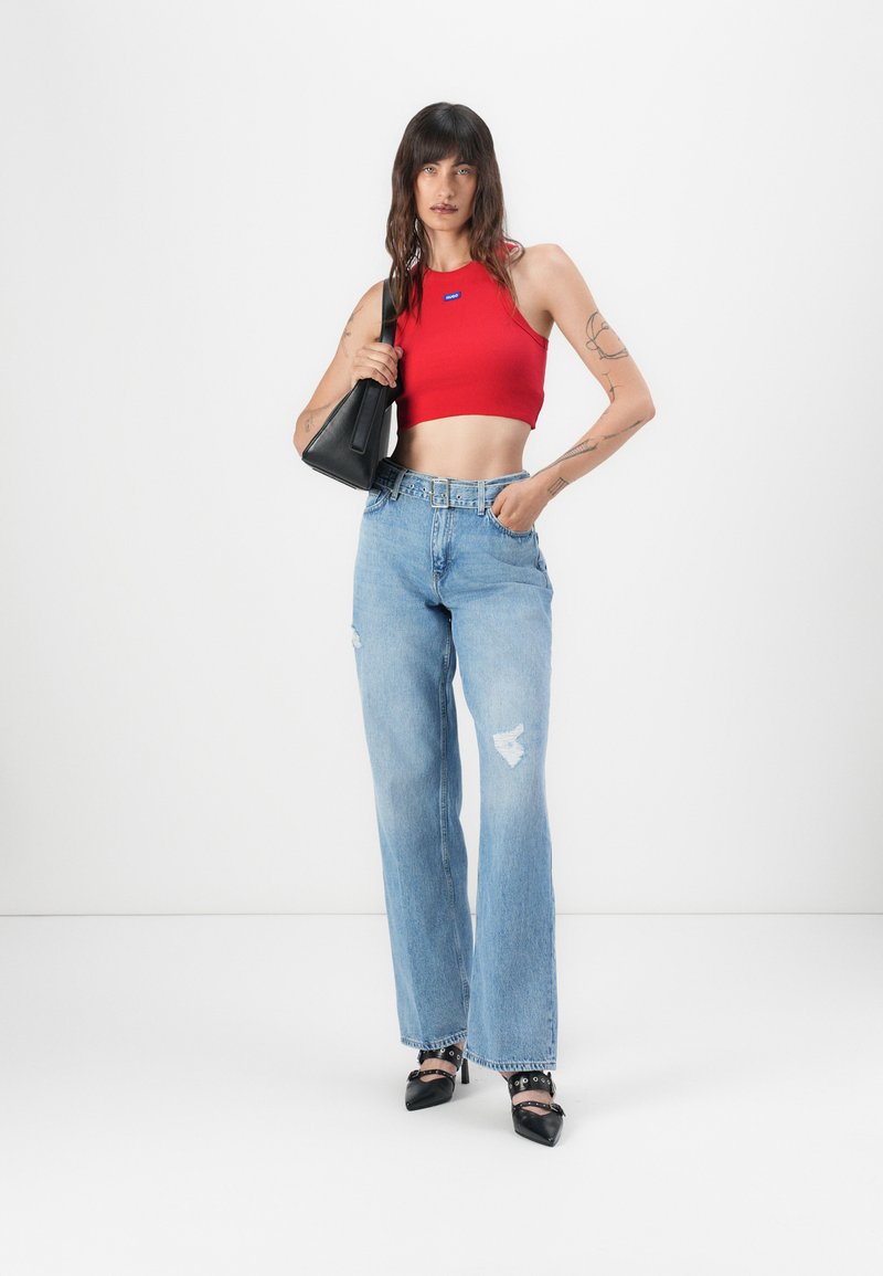 Top crop rouge, jeans taille haute bleu clair avec des déchirures, et chaussures à talons noires. Sac à main noir au design structuré.